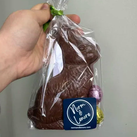 Chocolate bunny in clear plastic wrap with a blue label held by a hand against a plain background